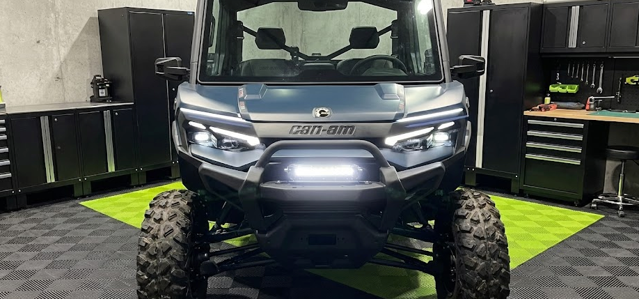 Front view of a Can-Am Defender UTV with a bright LED light bar mounted on the front bumper, demonstrating a clean, professional installation using the included hardware.
