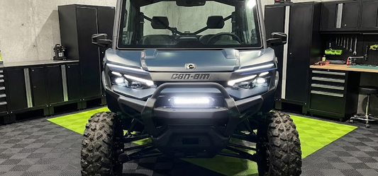 Front view of a Can-Am Defender UTV with a bright LED light bar mounted on the front bumper, demonstrating a clean, professional installation using the included hardware.