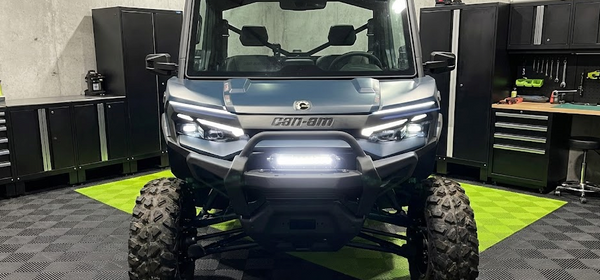 Front view of a Can-Am Defender UTV with a bright LED light bar mounted on the front bumper, demonstrating a clean, professional installation using the included hardware.
