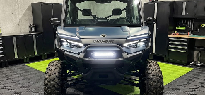 Front view of a Can-Am Defender UTV with a bright LED light bar mounted on the front bumper, demonstrating a clean, professional installation using the included hardware.