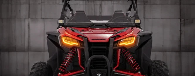 Front view of a red Honda Talon off-road vehicle, highlighting its aggressive design with bright amber headlights and suspension details, showcasing the vehicle's rugged appearance against a neutral background.